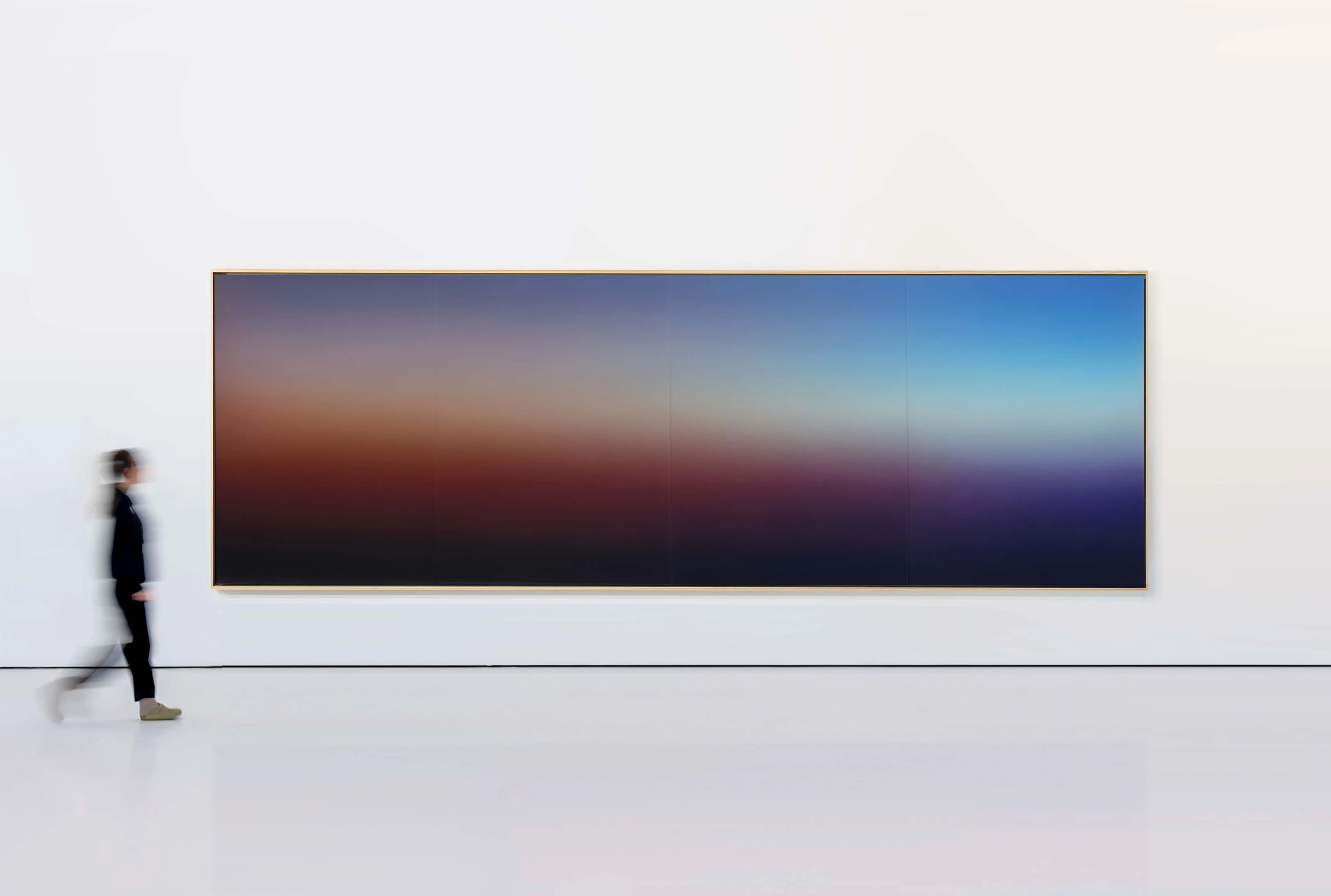 A panoramic painting spanning a gallery wall, a band of red and amber between dark blue above and below; a figure walking past gives its scale.